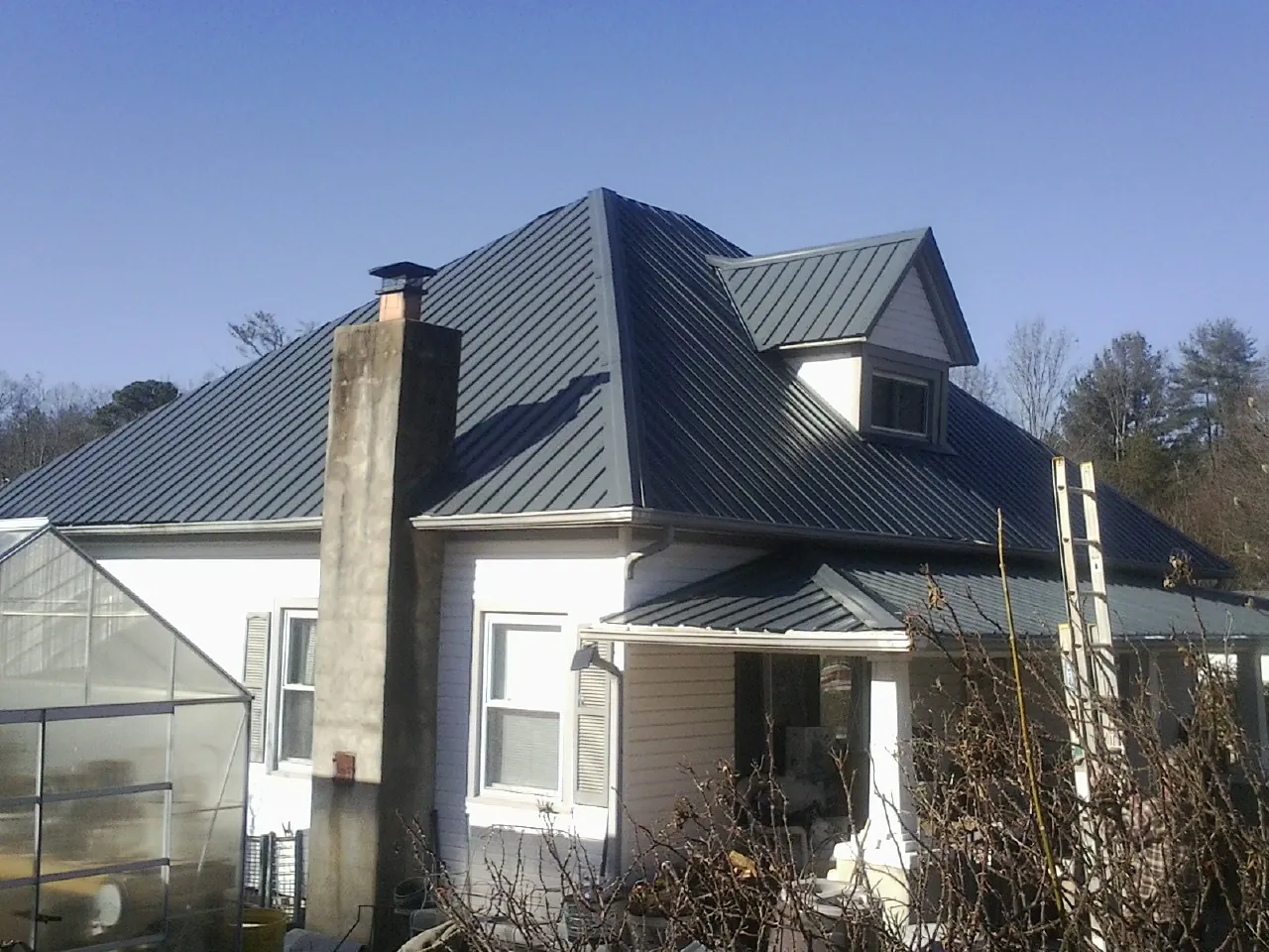 Dark blue standing seam metal roof on a white farmhouse with dormer — Slate & Tile Roof Repair by Roofing Brothers in Mc Lean