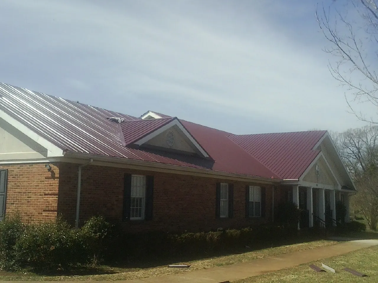 Red metal roof with gabled entries on a long brick building, from a Hail Damage Roof Repair job in Mc Lean