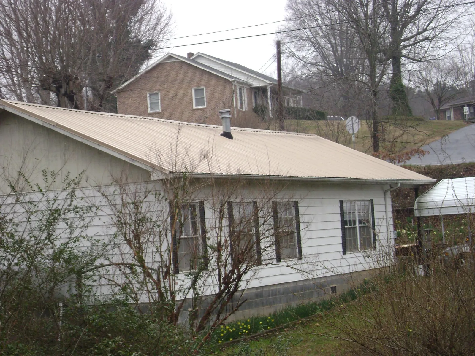 Tan metal roof on a white sided house set into a hillside — Commercial Roofing by Roofing Brothers in Mc Lean